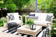 a modern country terrace with a deck, simple wooden furniture and printed textiles, a black side table and candle lanterns and greenery