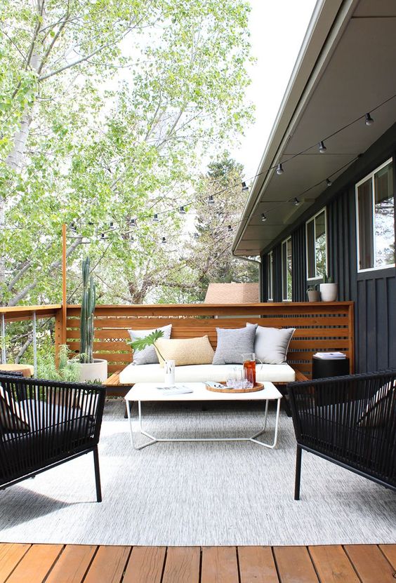 a modern country terrace with a wooden deck, a large rug, a sofa, rattan chairs, a small table and potted plants and cacti