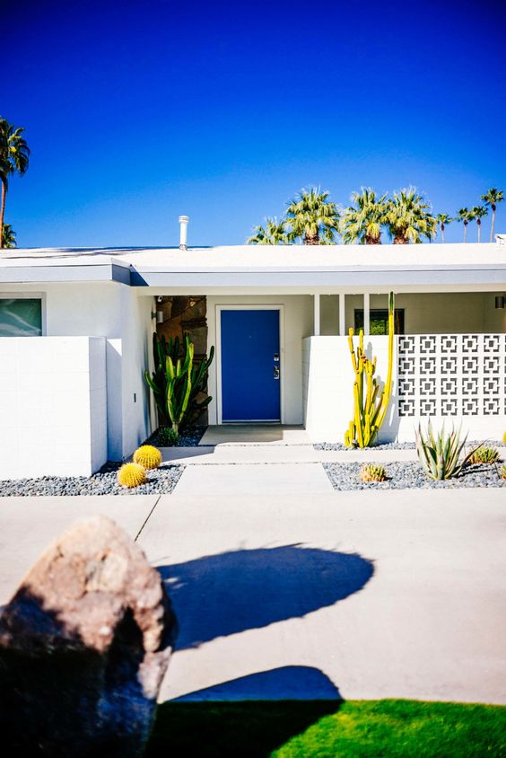 A modern desert entrance with a screen, a bold blue door, growing cacti and tiled pathways is a chic mid century modern space