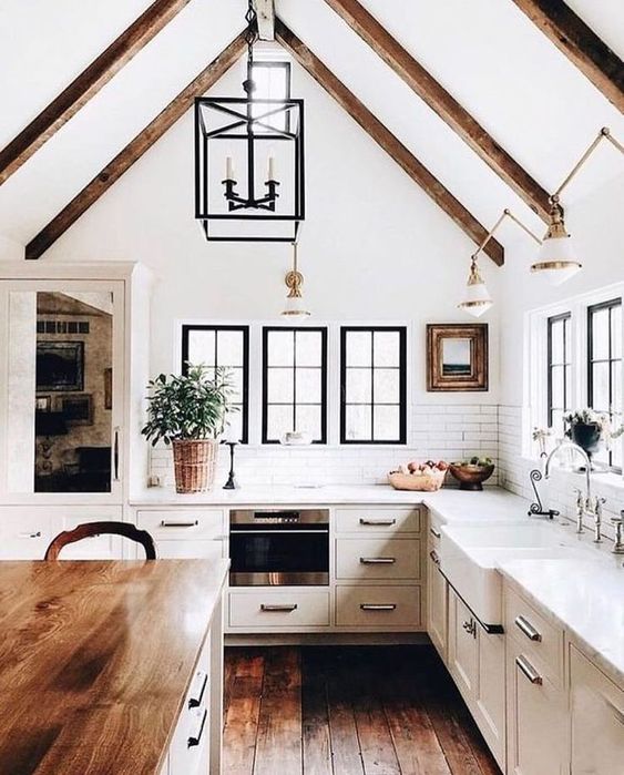 a modern dove grey country kitchen with dark wooden beams on the ceiling, pendant lamps and a kitchen island with a butcherblock countertop