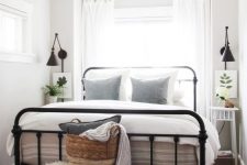 a modern farmhouse bedroom with a black forged bed, neutral nightstands and a bench, neutral bedding and a lovely basket