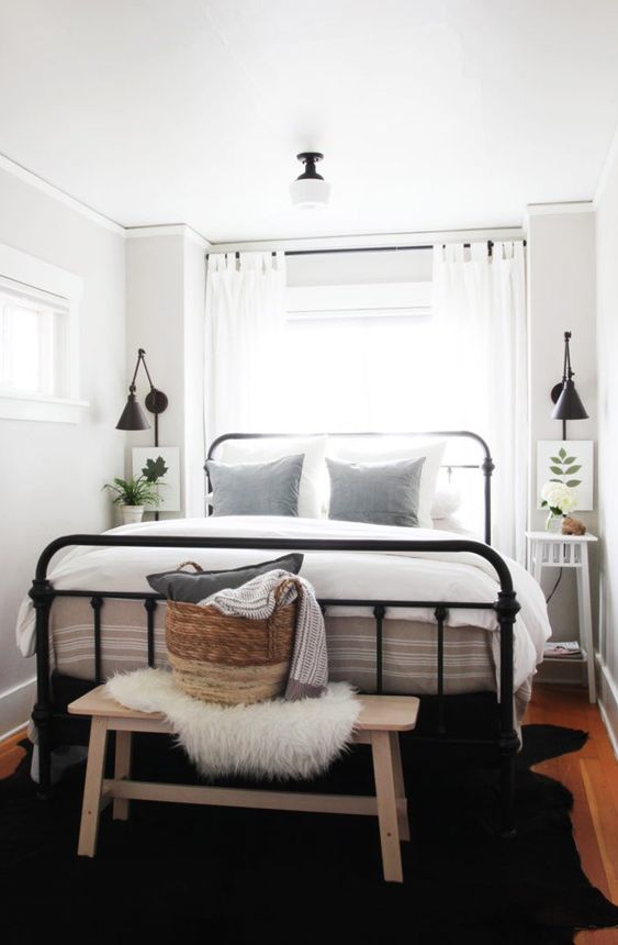 a modern farmhouse bedroom with a black forged bed, neutral nightstands and a bench, neutral bedding and a lovely basket