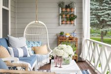 a modern farmhouse coastal porch with wicker furniture, a suspended egg-shaped chair, a coffee table, striped accessories, potted plants