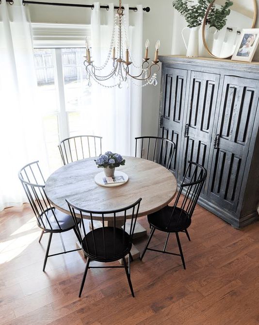 a modern farmhouse dining nook with a black storage unit, a stained round table, black chairs and a crystal chandelier