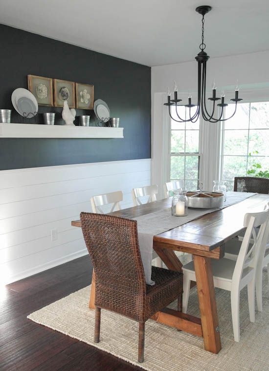a modern farmhouse dining room with a black wall and white planks, a stained dining table, mismatching chairs and a vintage chandelier