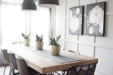 a modern farmhouse dining space with a grey paneled accent wall, a dining table with a thick tabletop, mismatching chairs and blakc pendant lamps