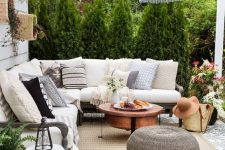 a modern farmhouse patio with a roof, a sectional, a copper coffee table, a woven ottoman, a pendant lamp and some plants