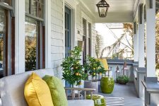 a modern farmhouse porch styled for summer, with simple wooden furniture, bright pillows, bold green side tables and potted trees