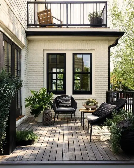 a modern front porch with a deck, black chairs with pillows, a side table, potted greenery and candle lanterns is cool