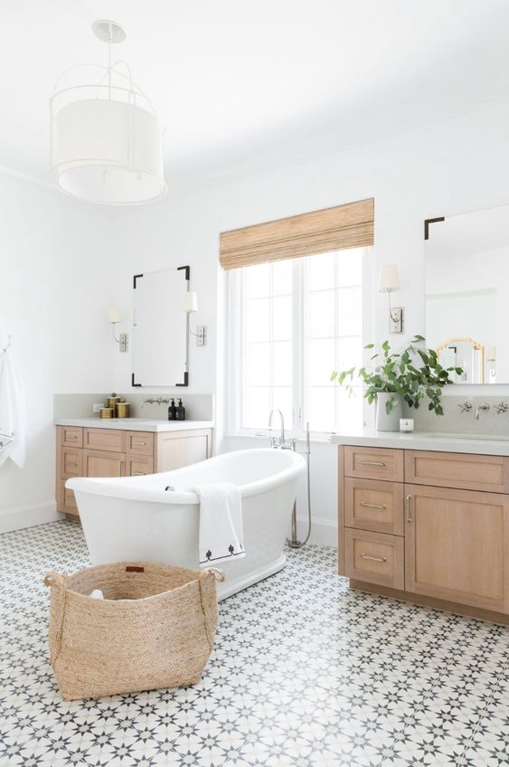 A modern rustic bathroom with a lovely patterned tile floor, stained vanities, a basket and shades plus a vintage inspired tub