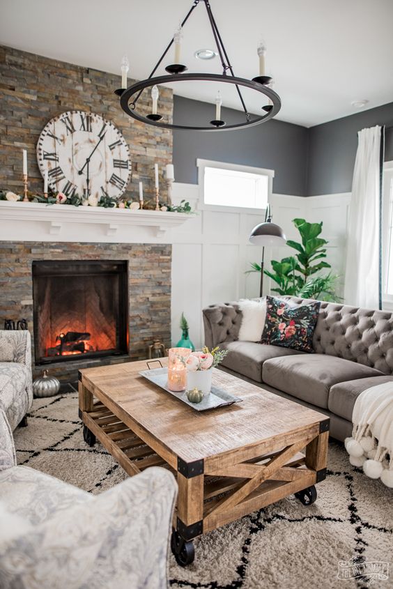 a modern rustic living room with a fireplace clad with faux stone, neutral furniture, a metal chandelier, a wooden coffee table