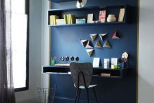 a navy accent wall that highlights the home office nook, with open shelves and geometric decor, with a floating desk and a grey chair