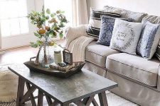 a neutral farmhouse living room with grey furniture, a wood and concrete coffee table, a large clock and printed textiles