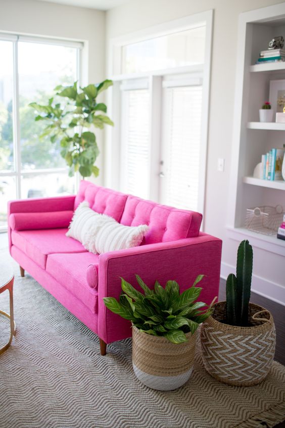 A neutral living room with a hot pink sofa for a color statement, potted plants in baskets and built in storage units