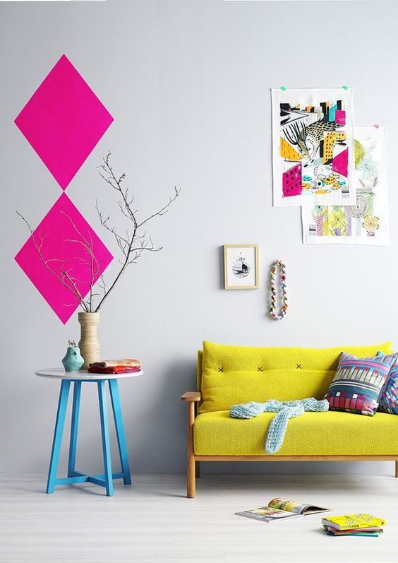 a pretty and bright interior with a lemon yellow loveseat, a table with blue legs, a colorful gallery wall and hot pink geometric decor