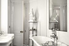 a refined and luxurious bathroom with white walls, a mosaic tile floor, a white vintage tub and an oversized mirror and a gold chandelier