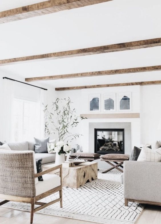 a refined modern country living room with a large fireplace, wooden beams, comfy furniture, a low wooden table and leather stools