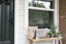 a simple modern front porch with a wooden bench and pillows, some potted greenery and succulents and a black door