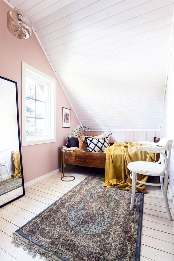 a small attic bedroom with a pink accent wall, a planked floor and ceiling, a wooden bed with some catchy bedding