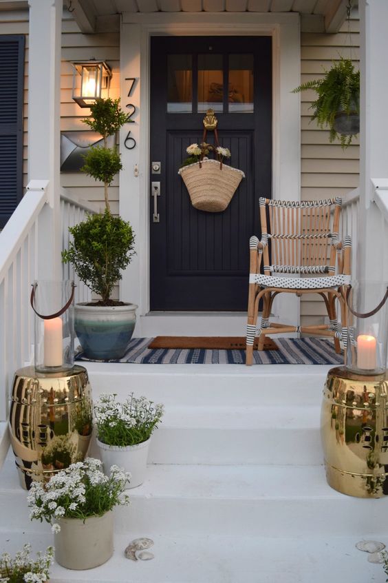 a small modern farmhouse porch with a rattan chair, shiny metallis side tables, potted blooms and greenery and a lantern