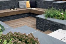 a small sunken outdoor space with a wooden deck, a built-in bench and growing plants and blooms is a lovely space to be