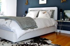 a sophisticated bedroom with a navy accent wall, a white upholstered bed, a cowhide rug, hairpin leg nightstands and some art