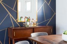 a sophisticated dining room with a navy geometric accent wall, stained furniture, grey chairs and a chic sunburst chandelier and a vintage console