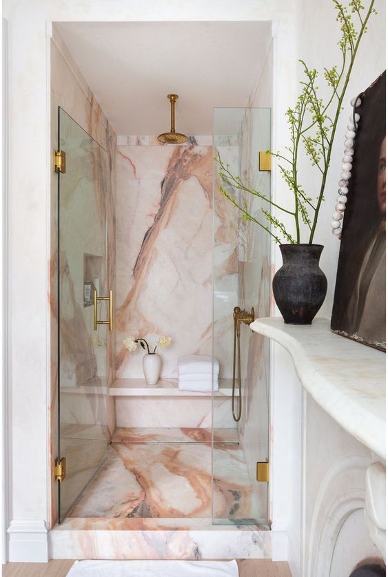 a sophisticated fancy bathroom with a gorgeous pink marble shower space, gold and brass touches and a fireplace right here