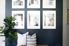 a stylish entryway with a navy accent wall, a bench with pillows, wooden candle lanterns, a black and white grid gallery wall and a potted plant