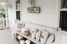 a white vintage farmhouse porch with neutral pillows, pumpkins, lanterns and a bag with firewood is styled for the fall in a lovely way