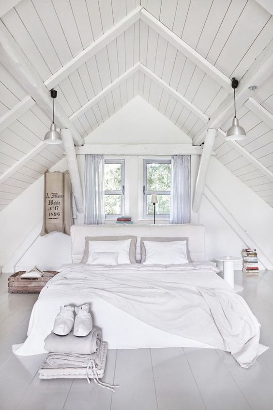 a whitewashed attic bedroom with an upholstered bed, mismatching nightstands, neutral and pastel bedding, pendant lamps