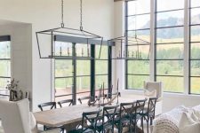 an elegant modern country dining space with lots of windows for the views, a stained table, black and white chairs and vintage chandeliers