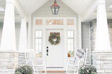 an elegant white farmhouse porch with a couple of white rockers and plaid textiles, potted blooms, candle lanterns and whitewashed pumpkins is amazing