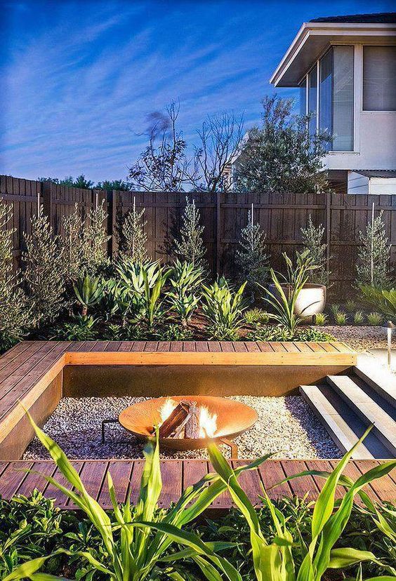 an outdoor sunken fire pit with gravel around and a deck that doubles as a bench around the pit is a cool modern solution
