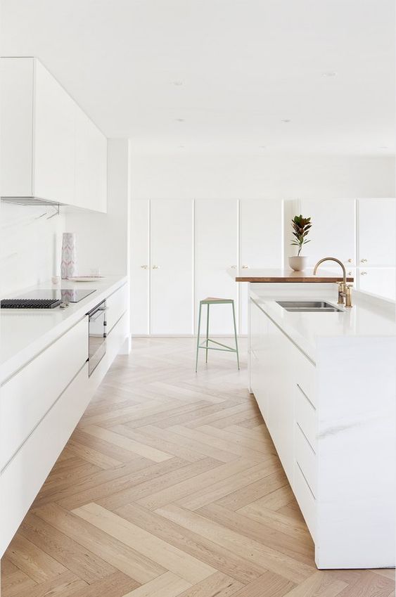 a minimalist white kitchen with sleek cabinets, a chevron floor and a butcherblock countertop, gold fixtures is a cool idea