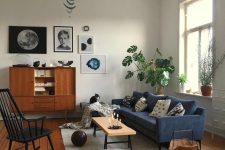 05 a mid-century modern living room with a navy sofa, a black rocker, potted plants, a stylish gallery wall and some cat furniture