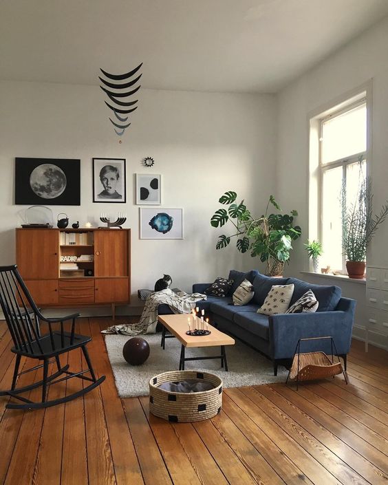 A mid century modern living room with a navy sofa, a black rocker, potted plants, a stylish gallery wall and some cat furniture