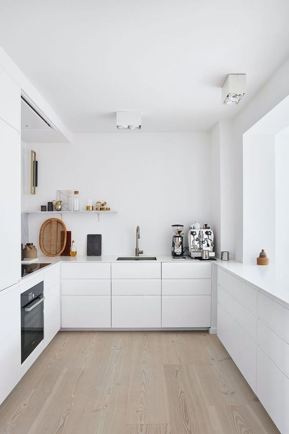 A minimalist white kitchen with sleek cabinets, sleek countertops, a shelf and built in appliances is a chic space