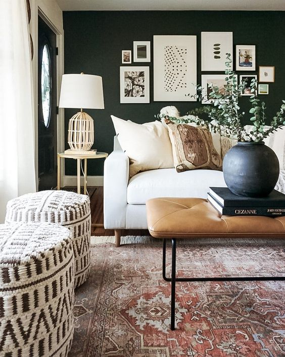 a chic black and white modern boho living room with a black accent wall, a white sofa, printed poufs, a leather ottoman and a cool gallery wall