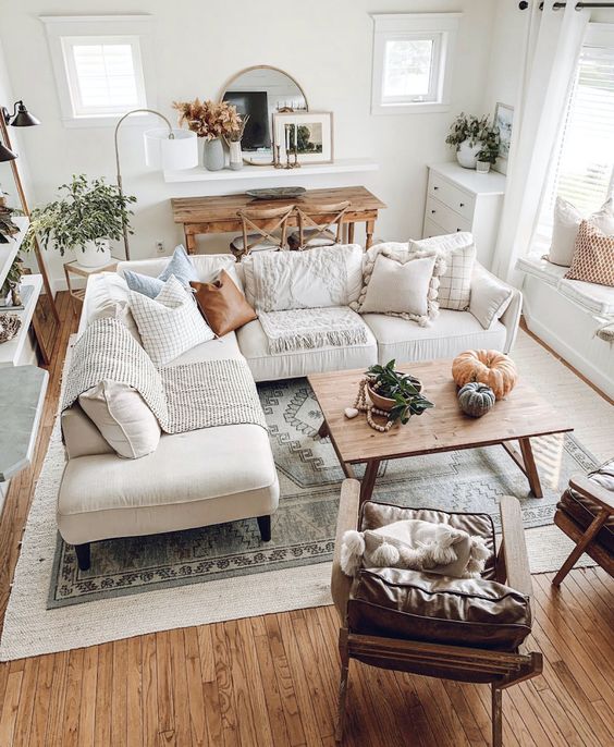 a neutral boho farmhouse living room with a white corner sofa, a wooden table, leather chairs, potted greenery and pumpkins