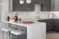 13 a refined kitchen with grey cabinets, a large kitchen island with a waterfall countertop, brass fixtures and gold pendant lamps