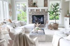 13 a white farmhouse living room with a fireplace clad with stone, white furniture, potted plants, neutral textules and views
