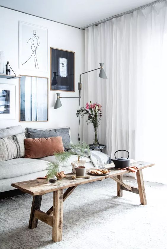 a Scandinavian living room with a neutral sofa, a wooden bench, a lovely gallery wall and grey sconces is chic