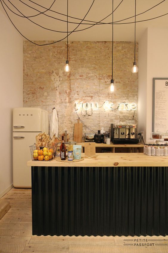 an industrial kitchen with a brick accent wall, a black kitchen island with a butcherblock countertops and wooden cabinets plus bulbs