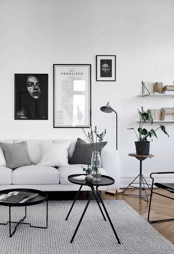 a laconic living room in Scandi style, with a white sofa, open shelves, black tables and a chair, black and white gallery wall