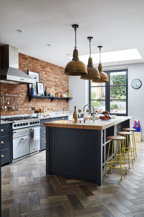 a chic kitchen with navy cabinets, a red brick wall, a navy kitchen island with a butcherblock countertop, metal pendant lamps