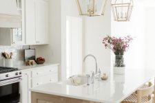 24 an elegant modern farmhouse kitchen with white cabinets, a light stained kitchen island, gold pendant lamps and woven chairs