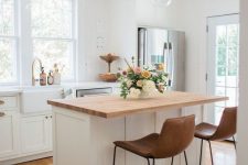 25 a pretty white farmhouse kitchen with shaker style cabinets, a small kitchen island with a butcherblock countertop and leather stools