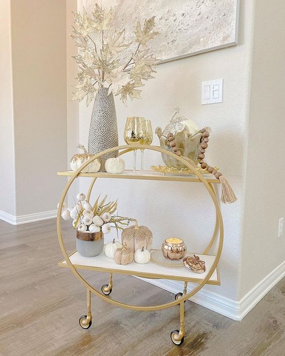 a lovely rounded gold bar cart on casters styled for the fall, with pumpkins, pampas grass, metallic leaves and wooden beads