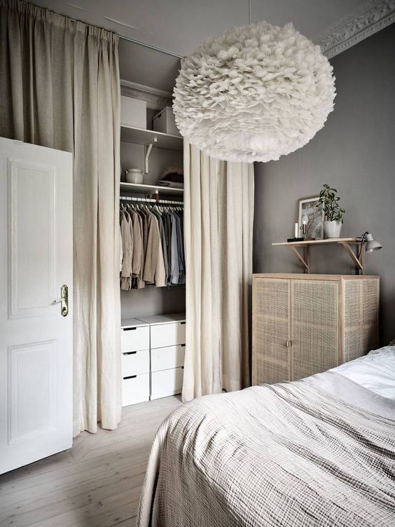a Scandinavian bedroom done in neutrals, with a cane dresser and a small closet organized in the corner and hidden with curtains